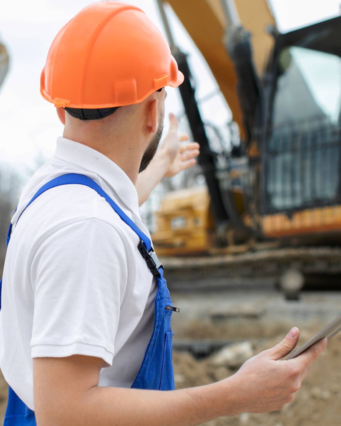 Bauarbeiter mit Schutzhelm vor einem Bagger auf der Baustelle